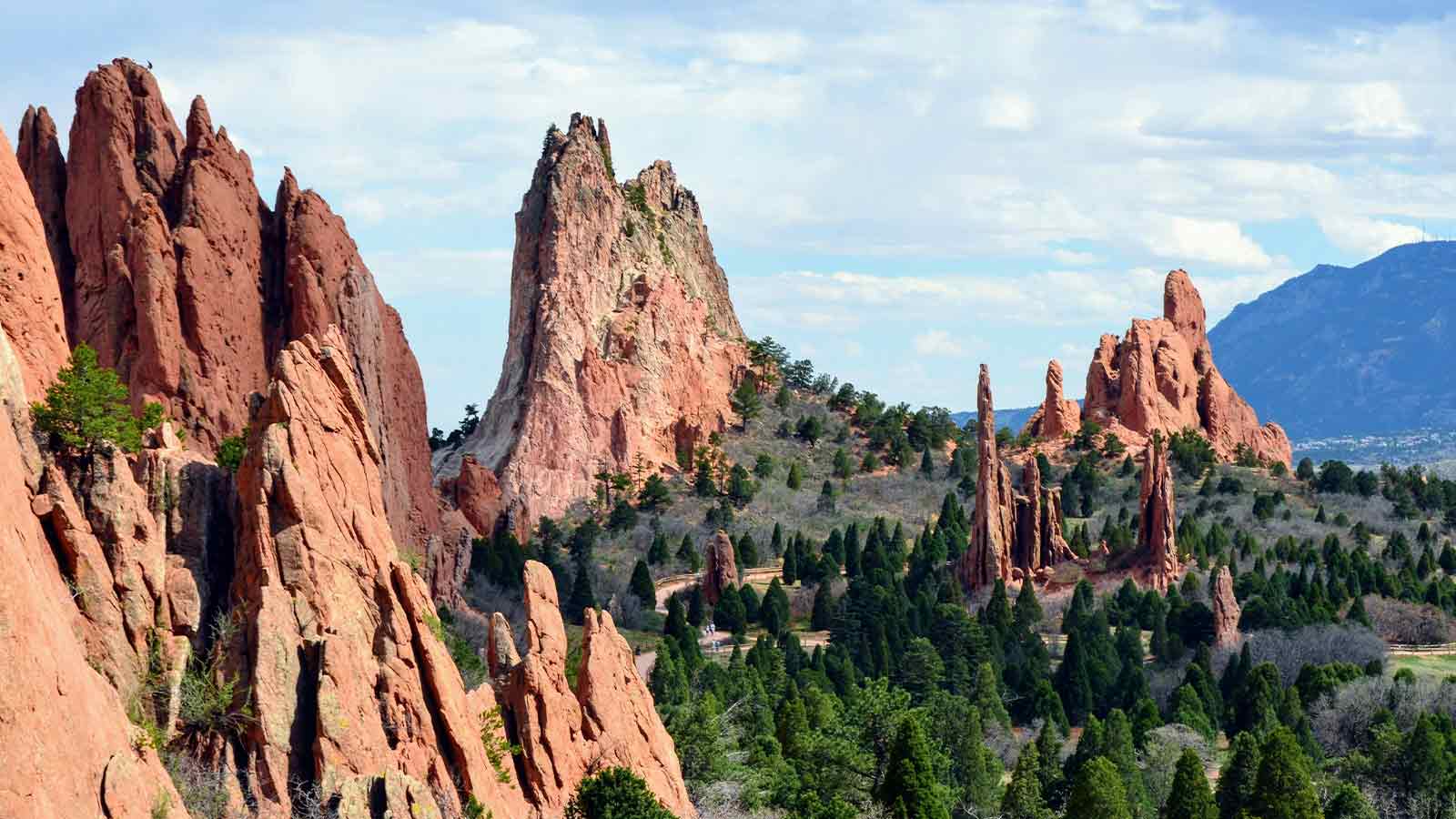 Red sandstone formations rising above conifers with a mountain ridge behind